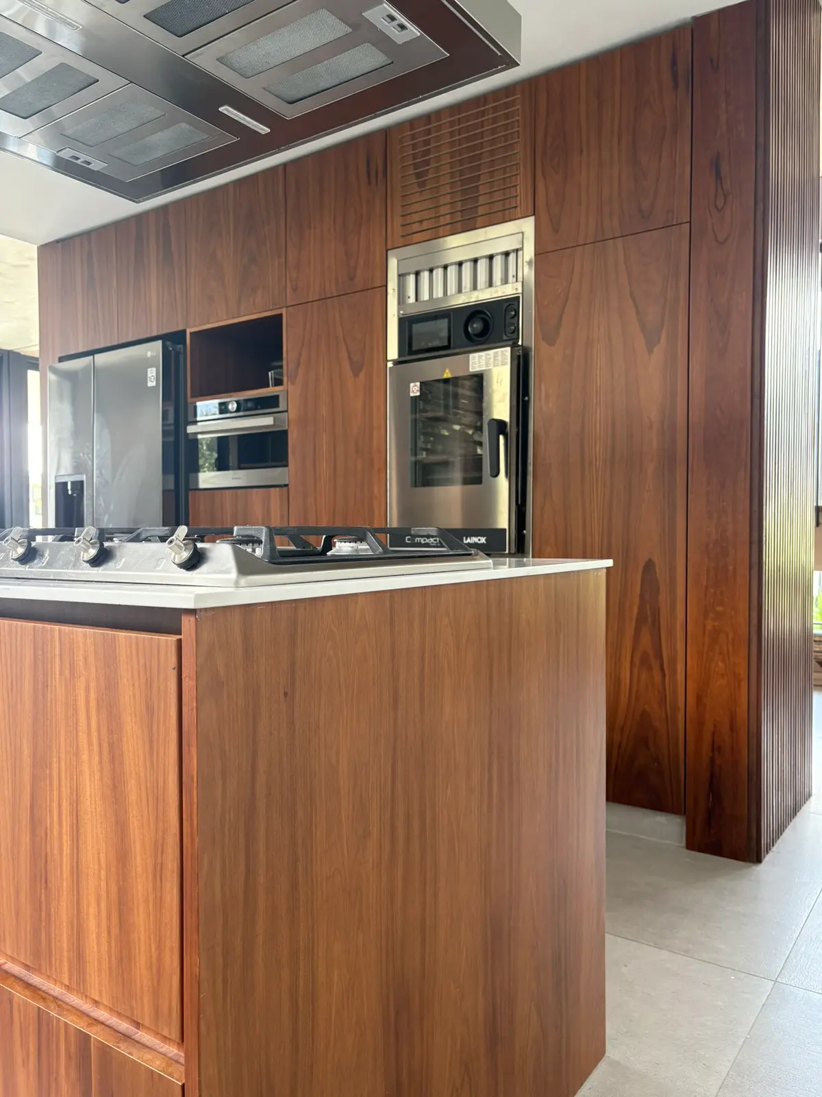 Cocina moderna con muebles y paredes de madera natural — proyecto Carpinchos - Estudio Gambotto, por ABEJA CONCEPT, en Nordelta