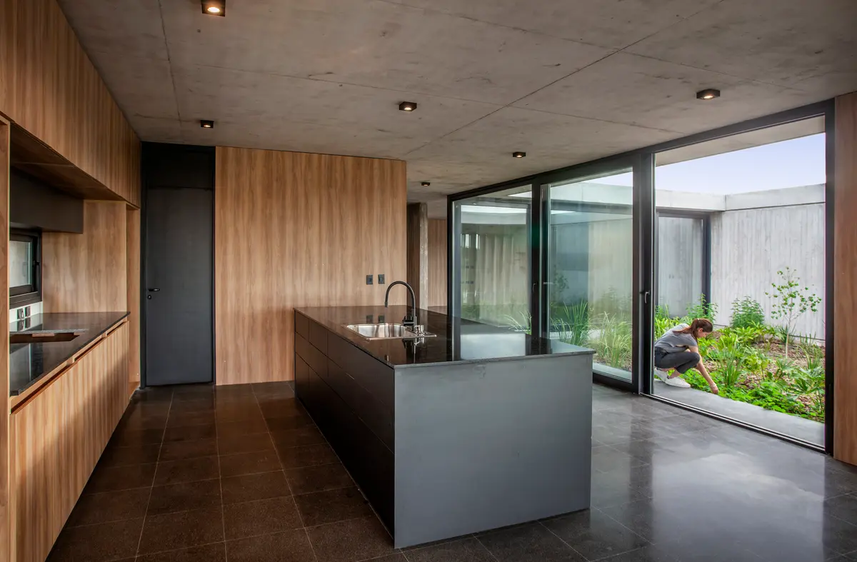 Cocina moderna con isla de hormigón y jardín interior — proyecto Casa JUMP, por V2 Arquitectos, en City Bell