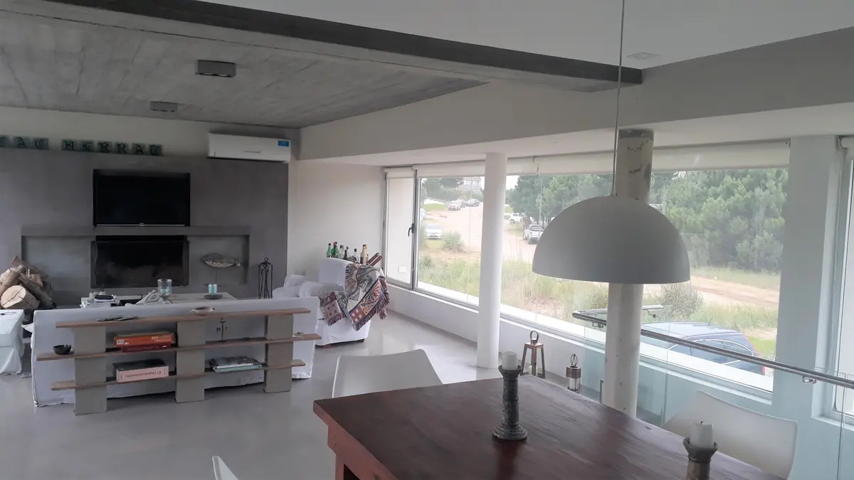 Living comedor moderno con concreto expuesto y grandes ventanales — proyecto VILLA ESMERALDA, por GJF estudio, en Pinamar