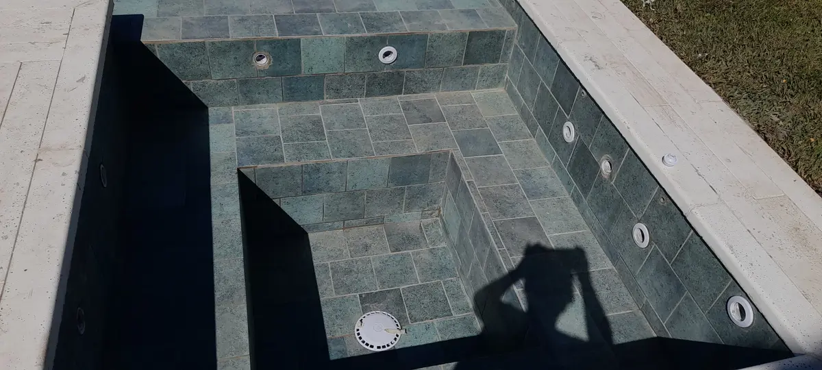 Pileta con revestimiento de piedra gris y escaleras integradas — proyecto piscina con hidromasaje, por Piscinas omar, en San Isidro