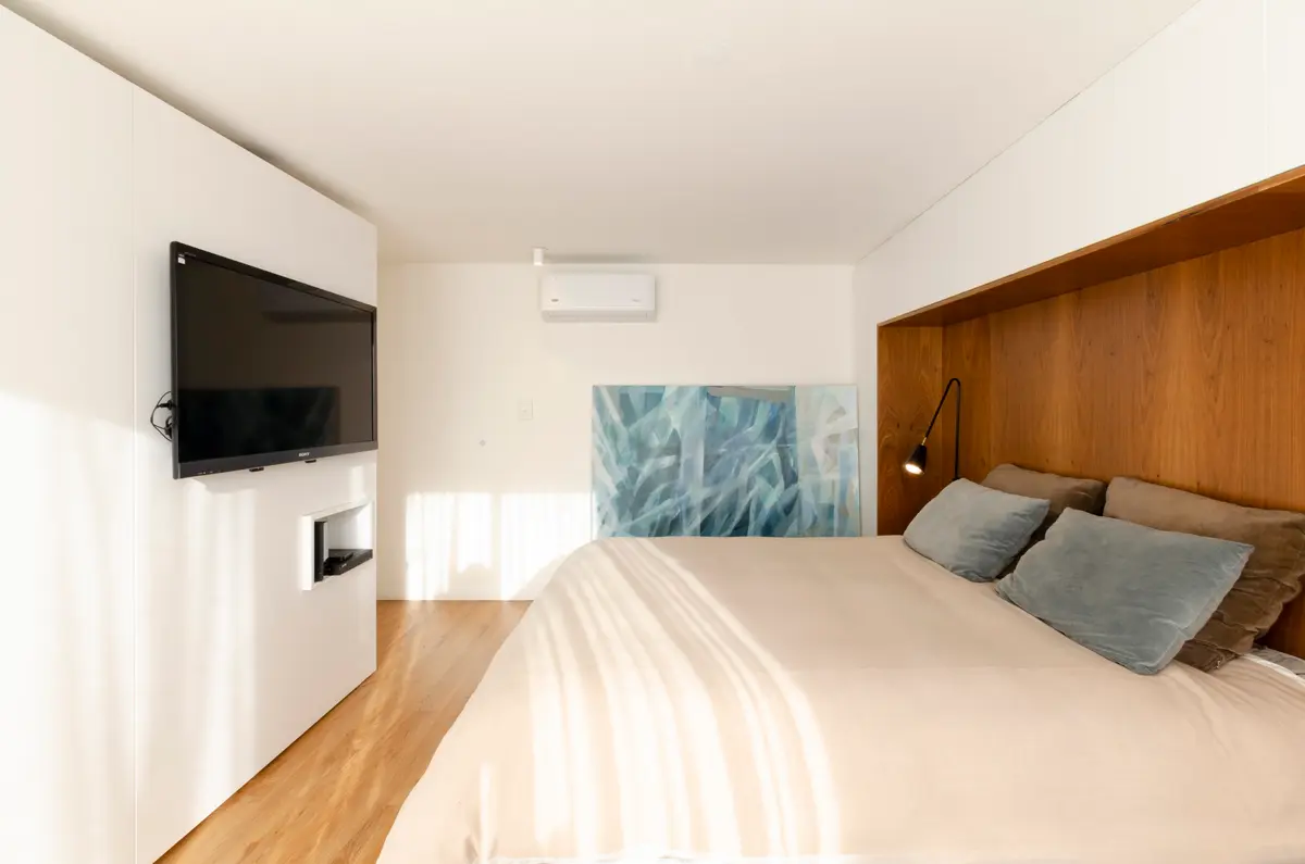 Quarto moderno com painel de madeira e TV embutida — projeto Guayra - Andrea Gonzales, por ABEJA CONCEPT, em Belgrano