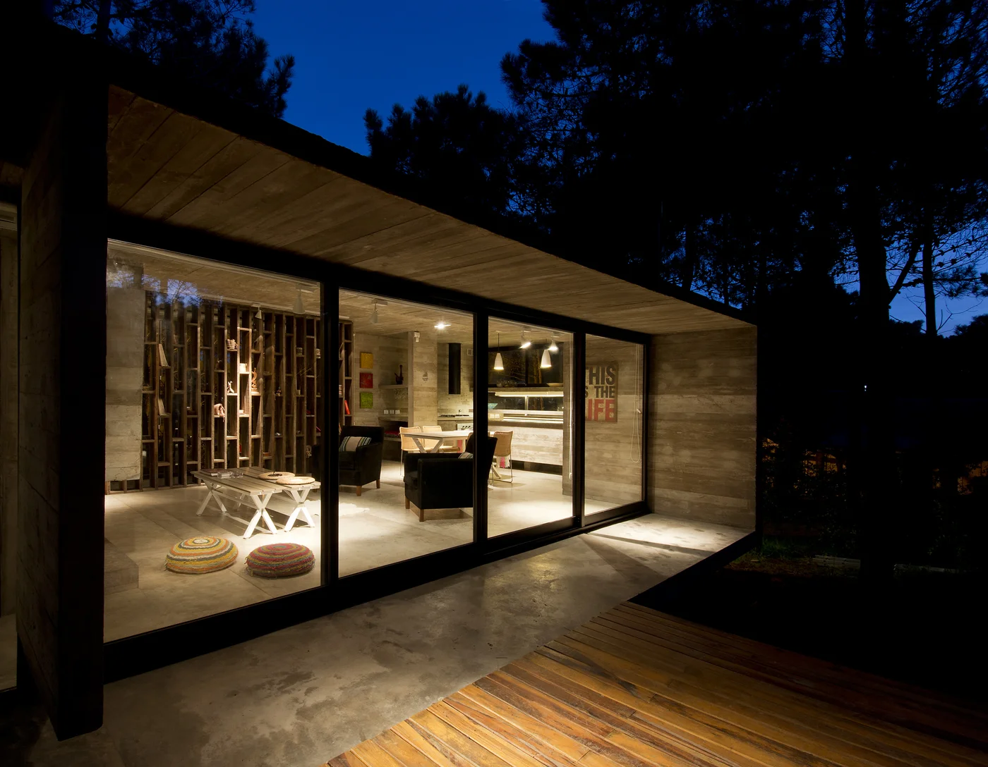 Galería moderna iluminada de noche entre árboles con deck de madera