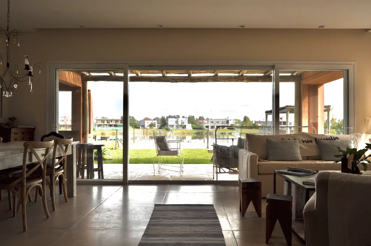 Living moderno con ventanal amplio y vista a lago y casas — proyecto Santa Teresa, Villanueva, por Marconi Silva Arquitectos, en Benavidez