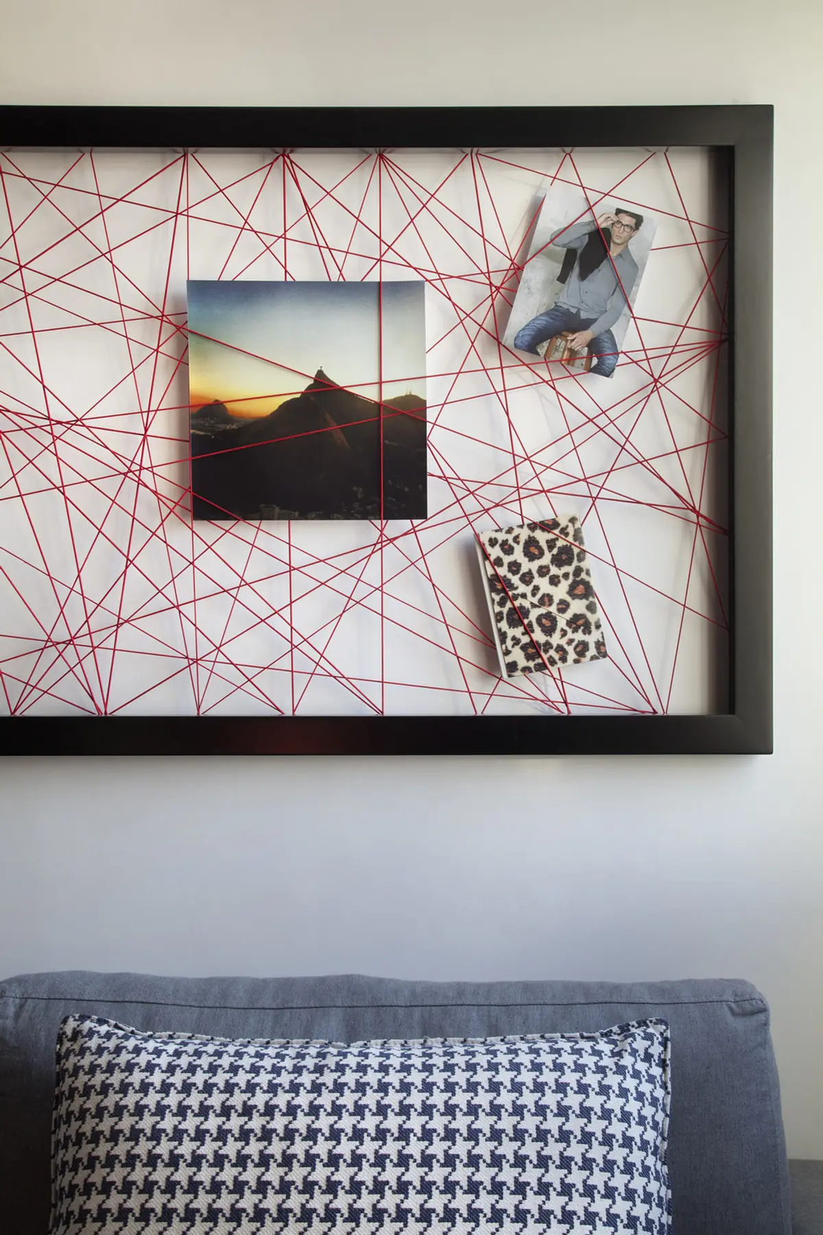 Marco negro con telaraña roja y fotos colgadas sobre sofá — proyecto RF House, por Studio Ro-ca