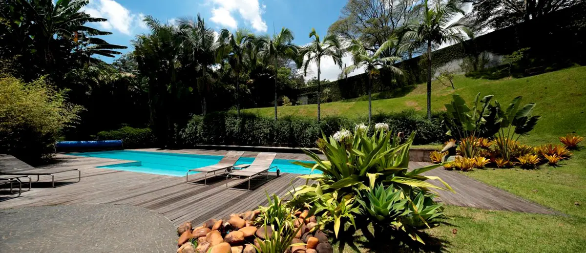 Piscina azul turquesa con deck de madera y jardín verde en ladera — proyecto Residência PU , por Gil Fialho