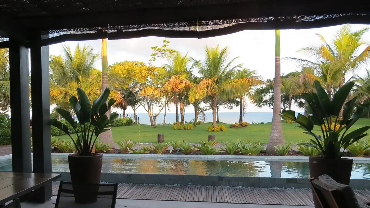 Terraza cubierta con vistas a laguna, palmeras y jardin paisajistico — proyecto Trancoso II, por Gil Fialho