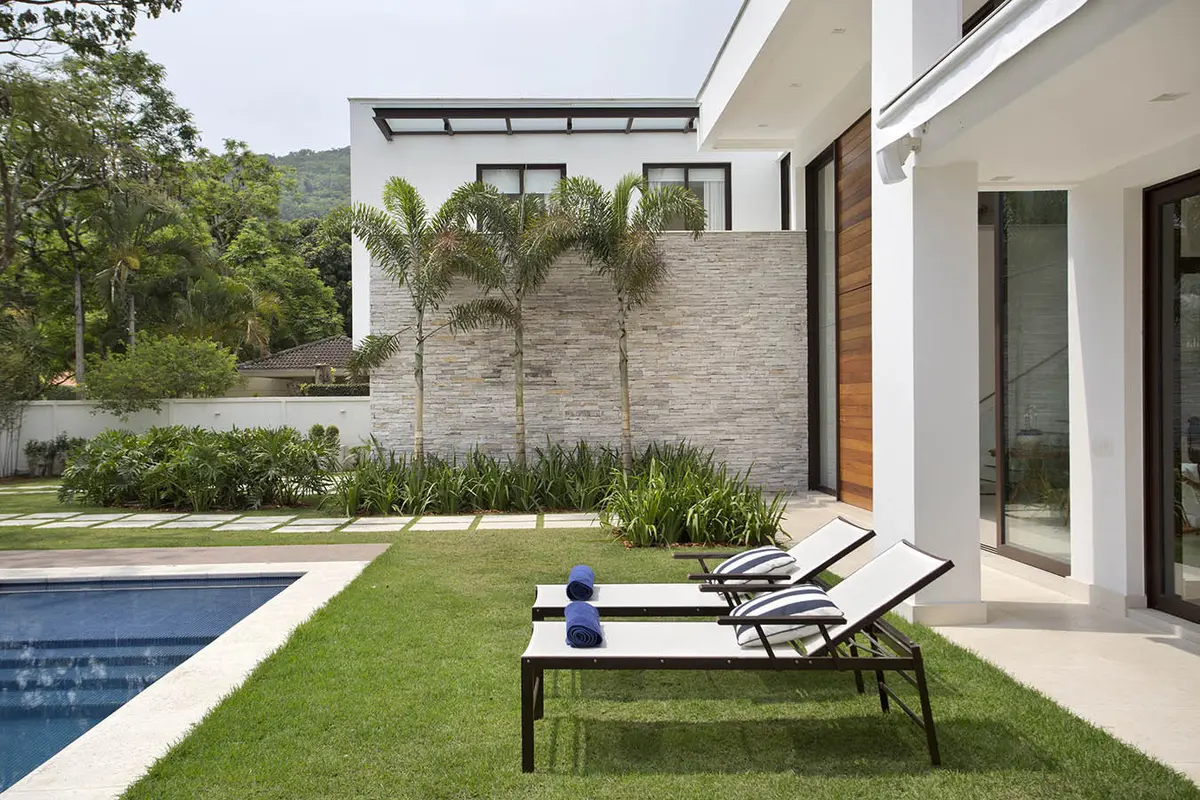 Pileta y living exterior de casa moderna rodeada de vegetación — proyecto Casa Jardim Ubá, por Amanda Miranda