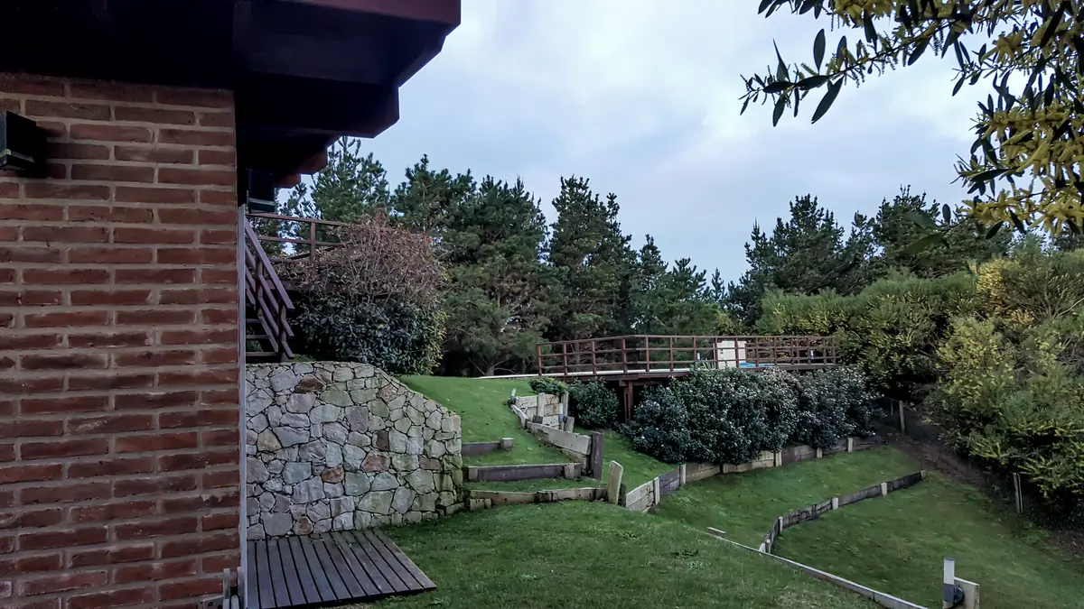 Fachada rústica com detalhes em pedra e tijolo, rodeada de jardim — projeto Vivienda Unifamiliar en Costa Esmeralda, por Estudio Schifano, em Costa Esmeralda