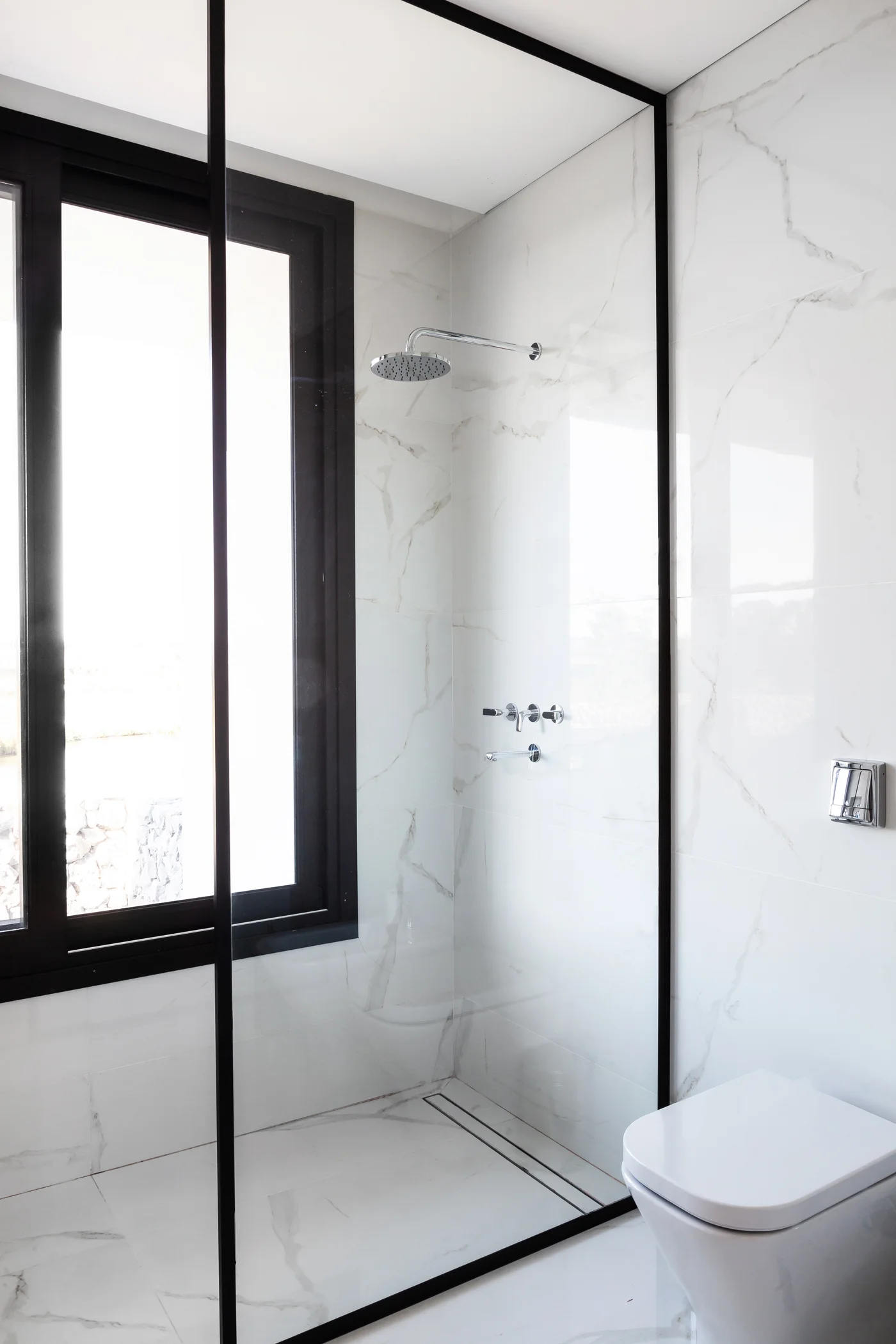 Baño moderno con ventana grande, mármol y ducha minimalista.
