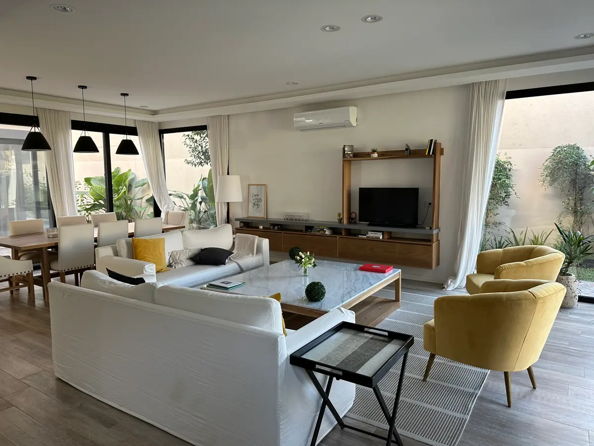 Sala de estar/jantar moderna com sofá modular, janelas amplas e detalhes amarelos — projeto Casa Belen, por Arq. Damian Fainzilber, em San Isidro