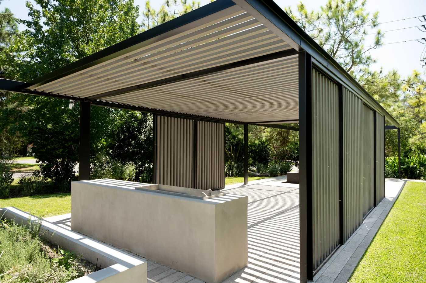 área de parrilla exterior moderna con barra de hormigón y pérgola