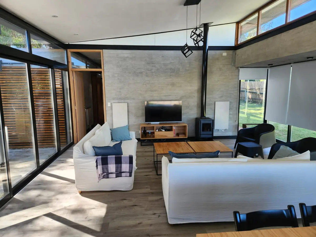 Sala de estar moderna com janelas amplas, concreto aparente e móveis brancos — projeto Casa Arenas del Sur, por Arq Fernando Ossvald, em Mar del Plata