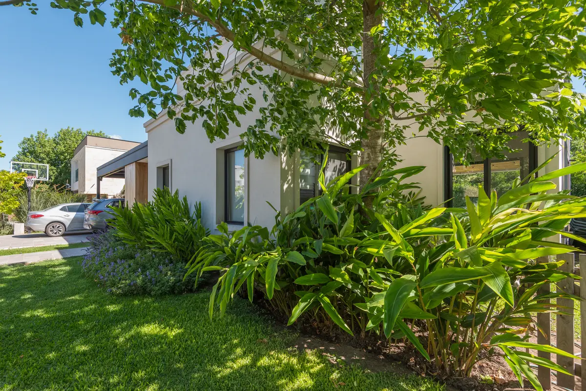 Fachada moderna branca com jardim exuberante e detalhes em madeira escura — projeto CASA GM, por IMF INÉS MARTINEZ FERRARIO