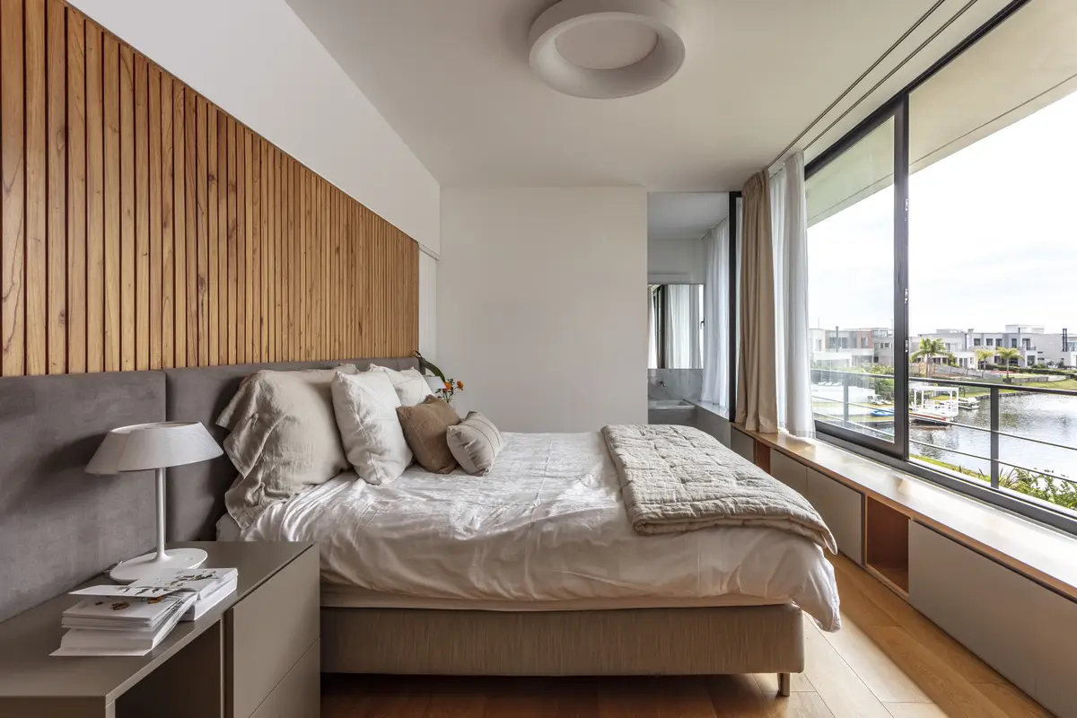 Quarto moderno com vista para o mar e parede de ripas de madeira — projeto Nordelta, por Judith Babour, em Nordelta
