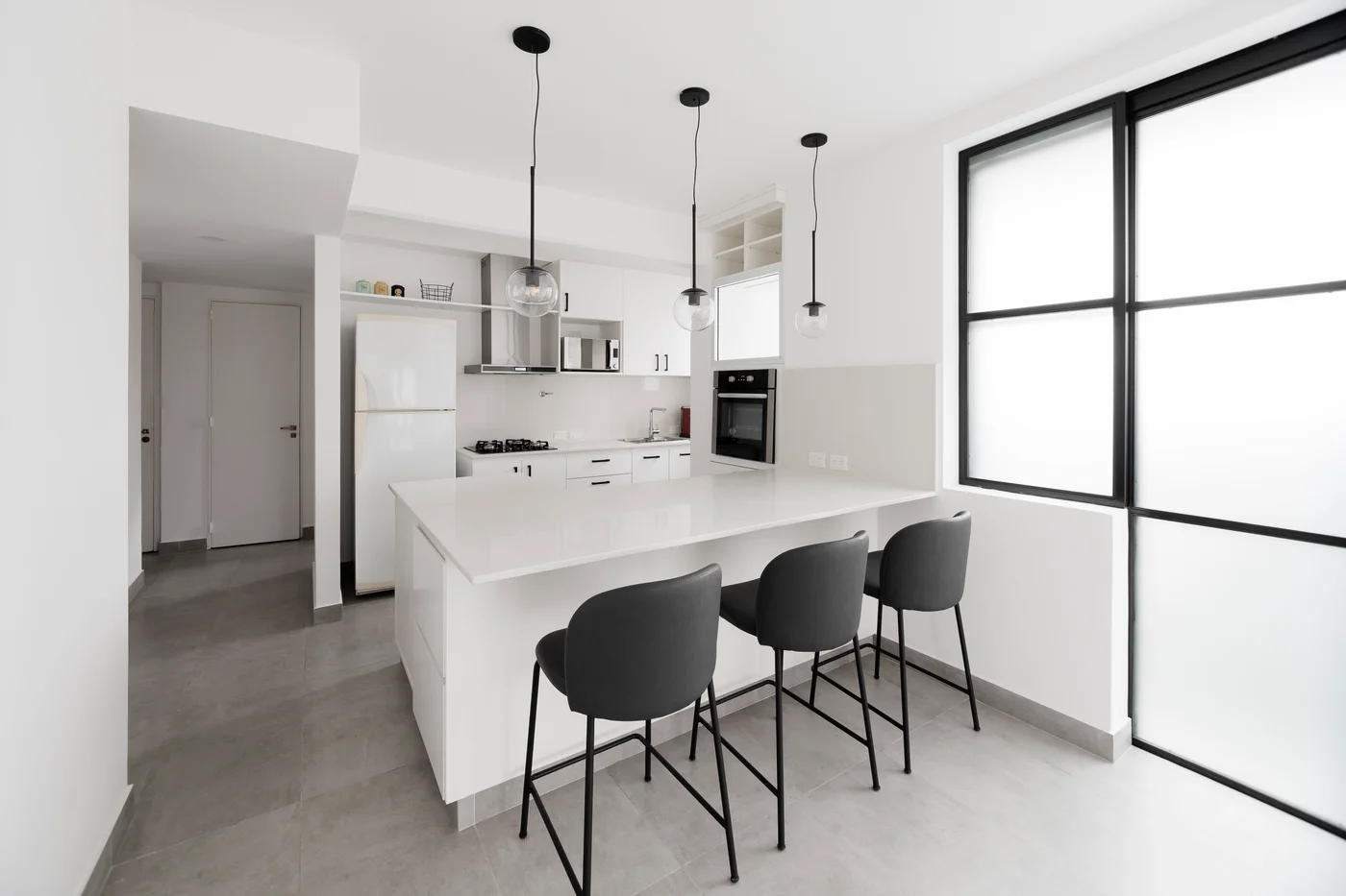 Cocina moderna minimalista con isla grande y luces colgantes negras.