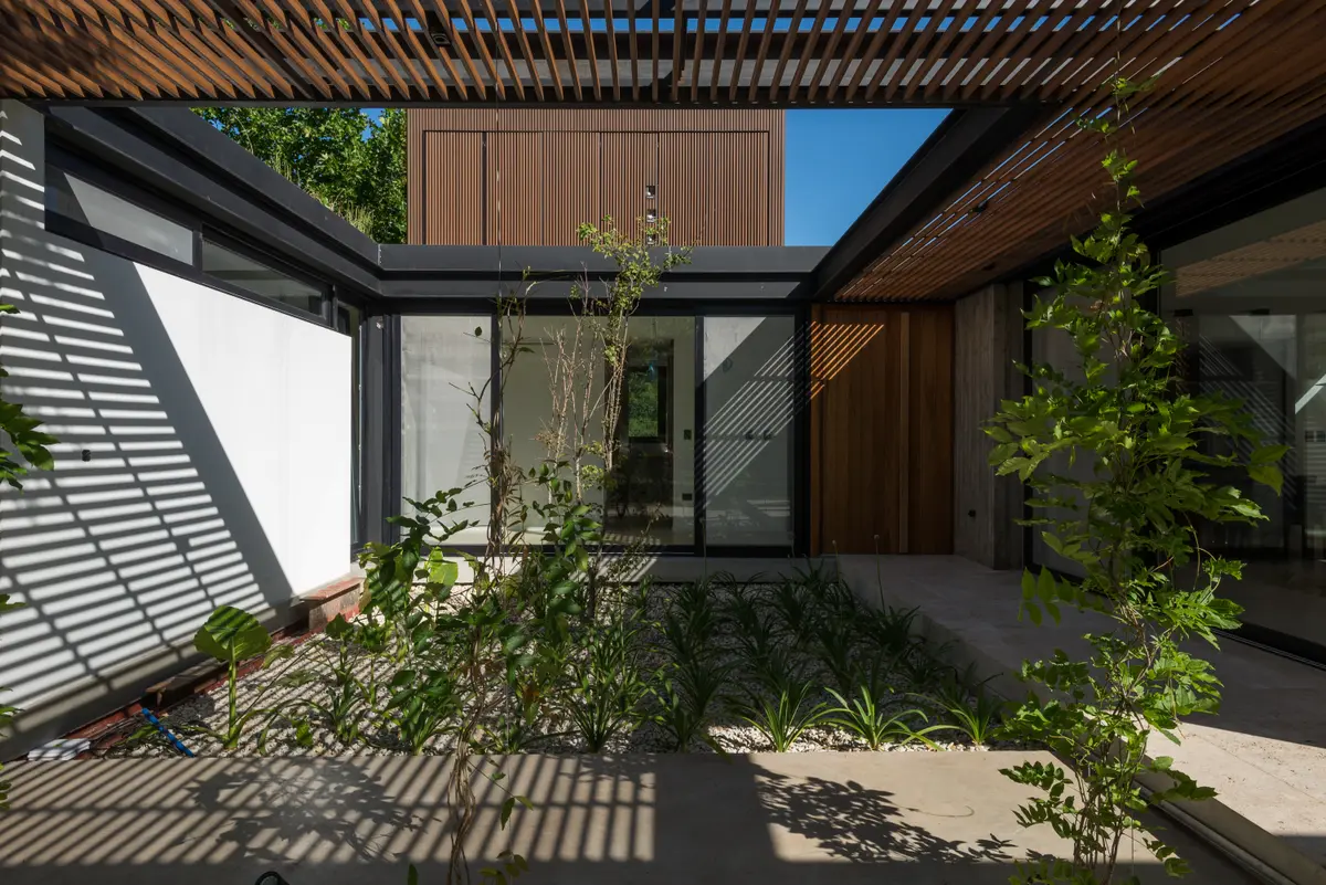 fachada moderna con pérgola de madera y vegetación — proyecto CASA AC , por BUSCETTI & DI BERNARDO arquitectas, en Villa Elisa