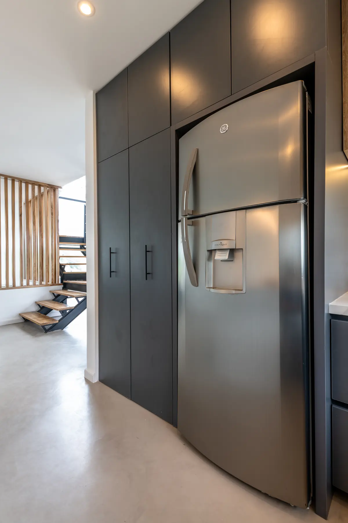 Cocina moderna con muebles grises integrados y escalera flotante — proyecto Santa Isabel - Andrea Gonzalez, por ABEJA CONCEPT, en Nordelta