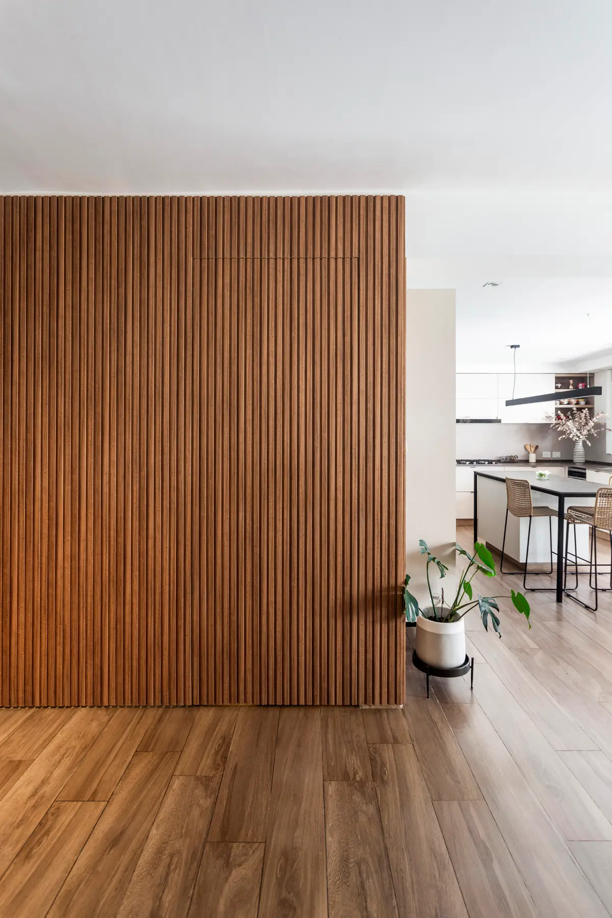 Sala de estar moderna com parede de ripas de madeira e cozinha integrada — projeto Casa en Martinez, por JT ARQUITECTURA, em Martínez