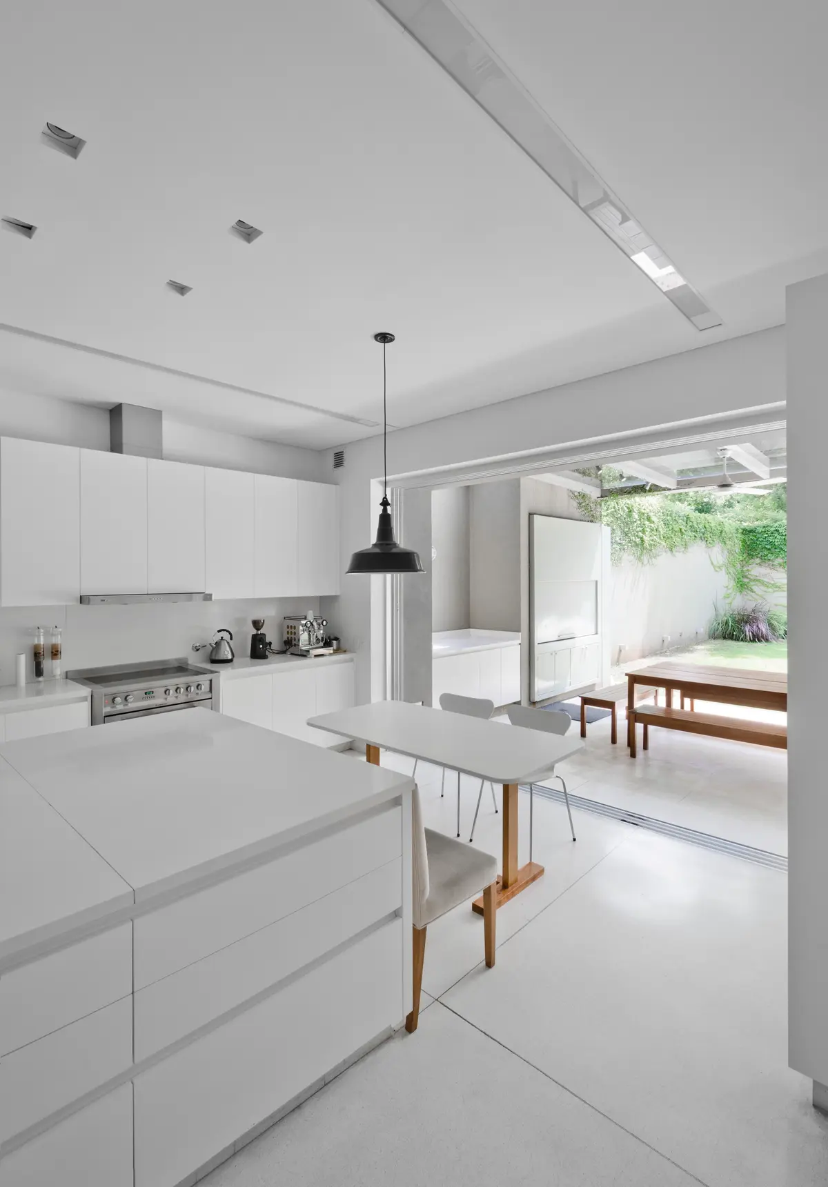 Cocina moderna blanca con isla, comedor integrado y acceso al exterior — proyecto Casa D, por Estudio Dado, en Belgrano