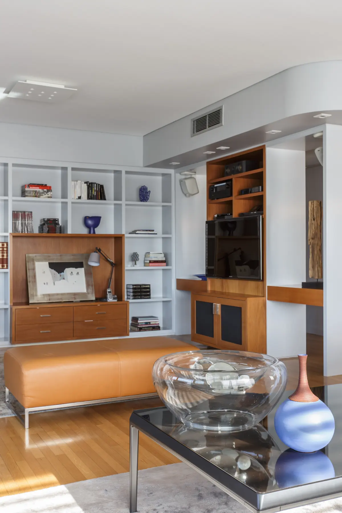 Sala de estar moderna com estantes e pufe de couro — projeto Piso en Belgrano, por Gutman+Lehrer Arquitectas, em Belgrano