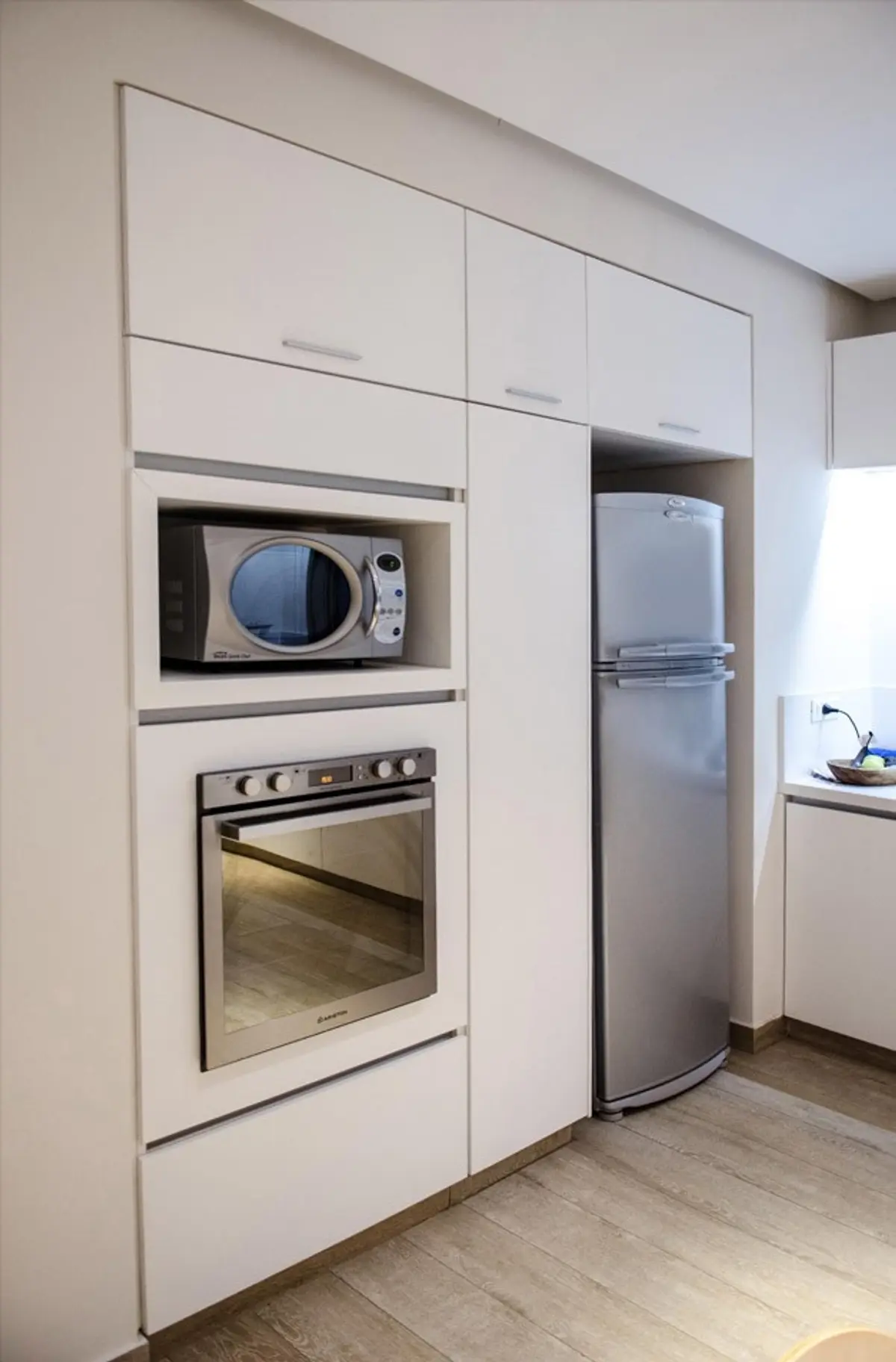 Cocina moderna blanca con electrodomésticos integrados y suelo de madera — proyecto Casa Nordelta, por linearecta.arquitectura, en Nordelta