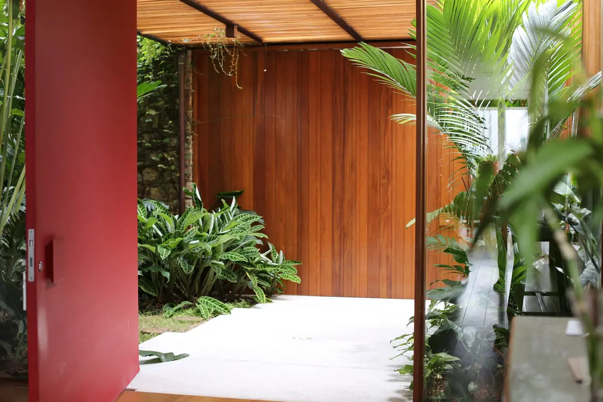 Patio con pergola de madera, columna bordo y vegetación tropical — proyecto Residência MP, por Gil Fialho