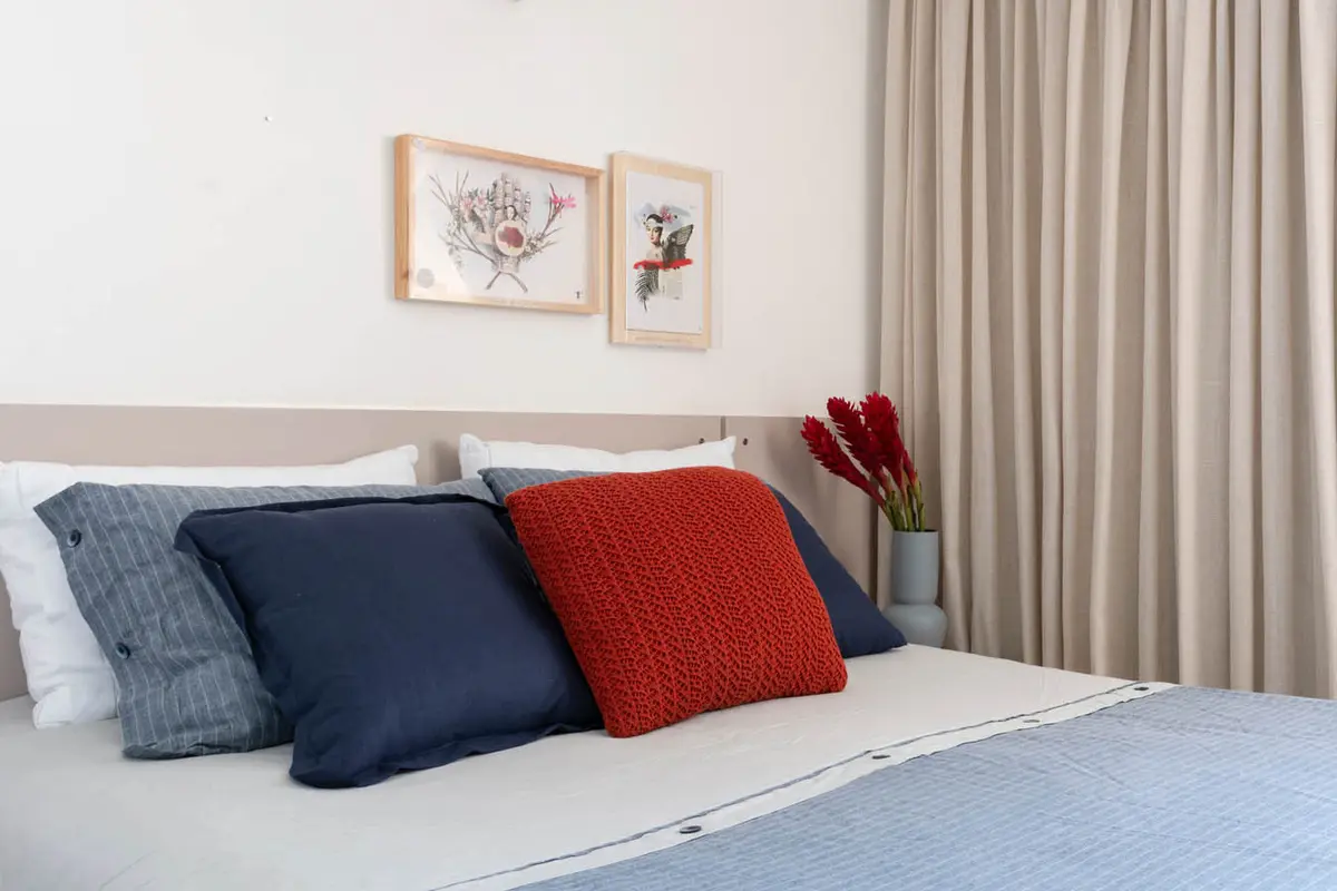 Dormitorio moderno con cama, almohadas azules y rojas, cortinas beige — proyecto Apartamento Santa Rosa, por Amanda Miranda