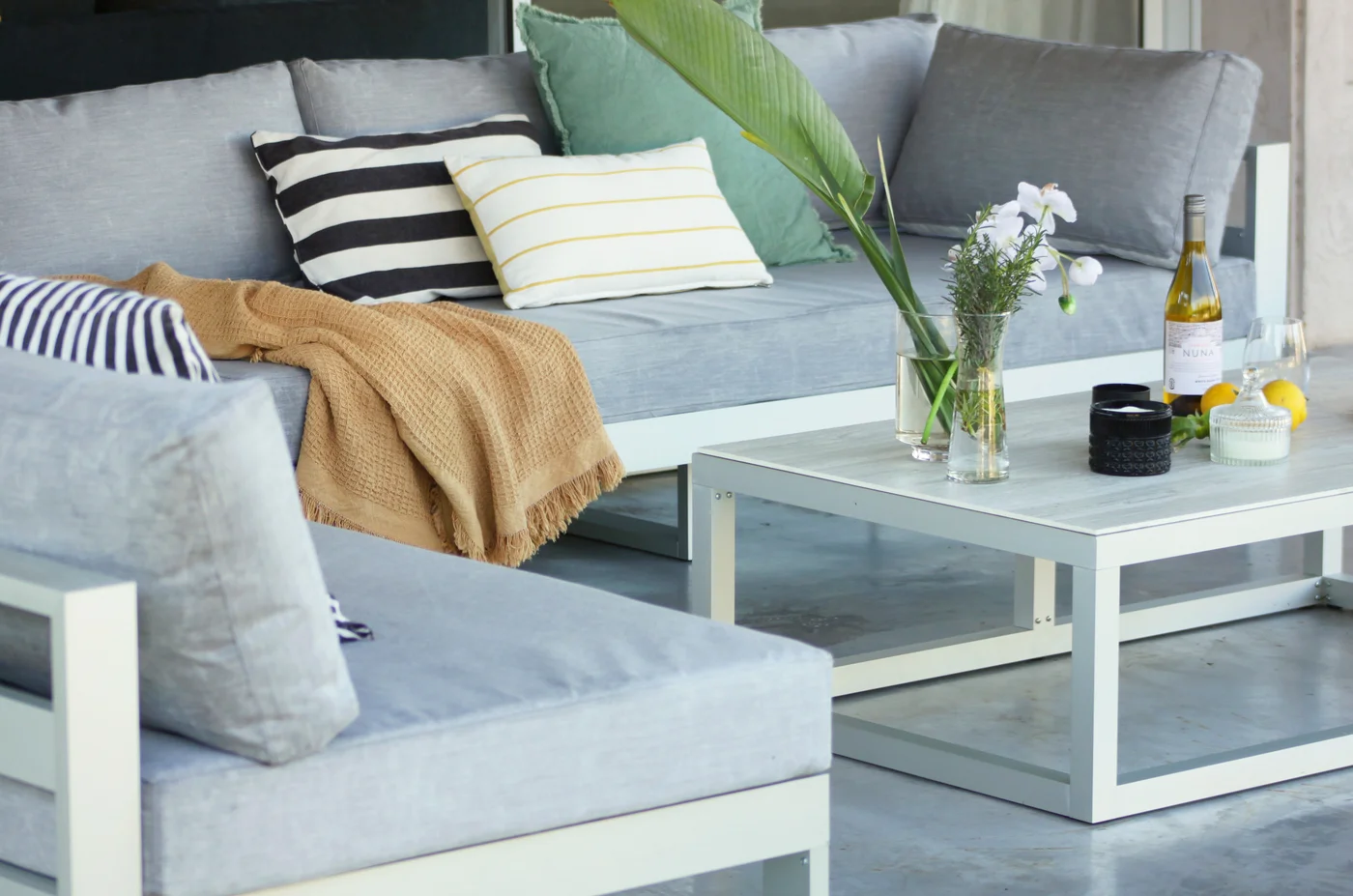 Living exterior moderno con sillón gris, mesa blanca y plantas.