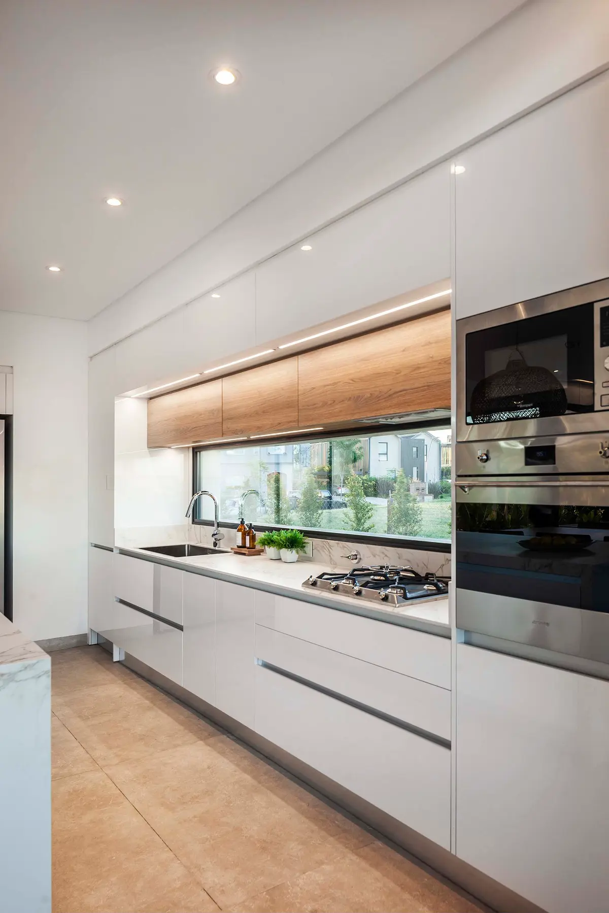 Cocina moderna con ventana larga, muebles blancos y de madera — proyecto CASA J2M, por GMARQ, en Belén de Escobar