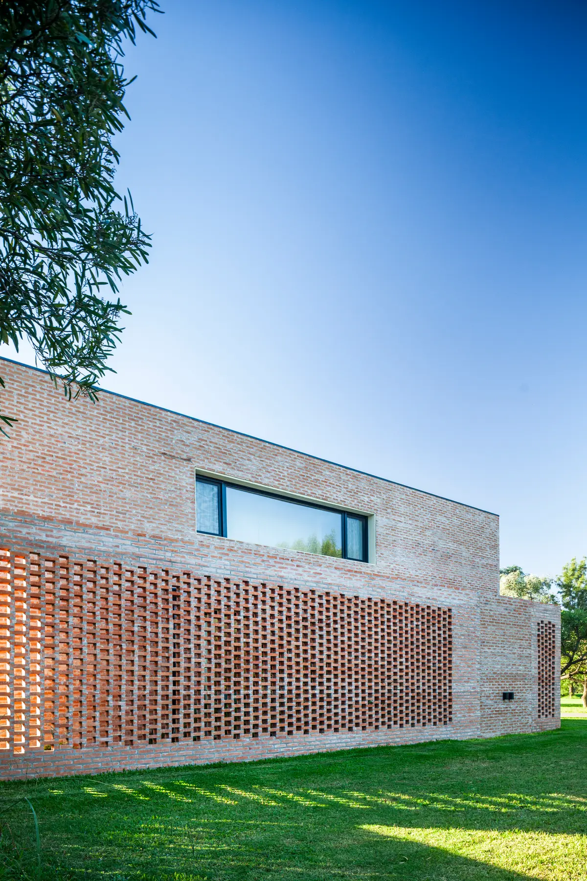 Fachada moderna de ladrillo visto con pantalla de ladrillo perforado y ventana alargada — proyecto Casa Brick, por LSA. , en Pilar