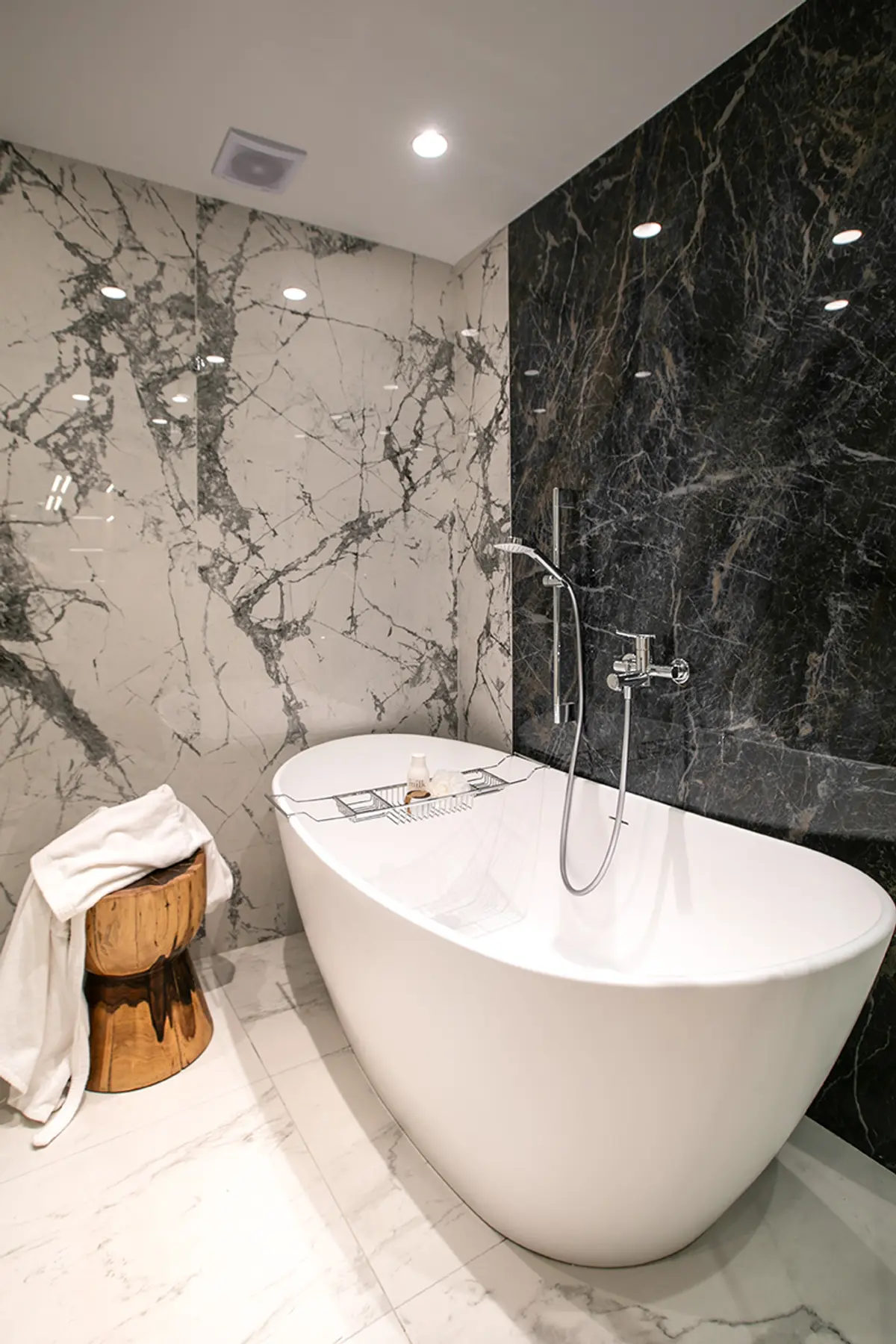 Baño moderno con bañera blanca y revestimiento marmol negro y beige — proyecto Casa Oroño, por Estudio Plats, en Buenos Aires