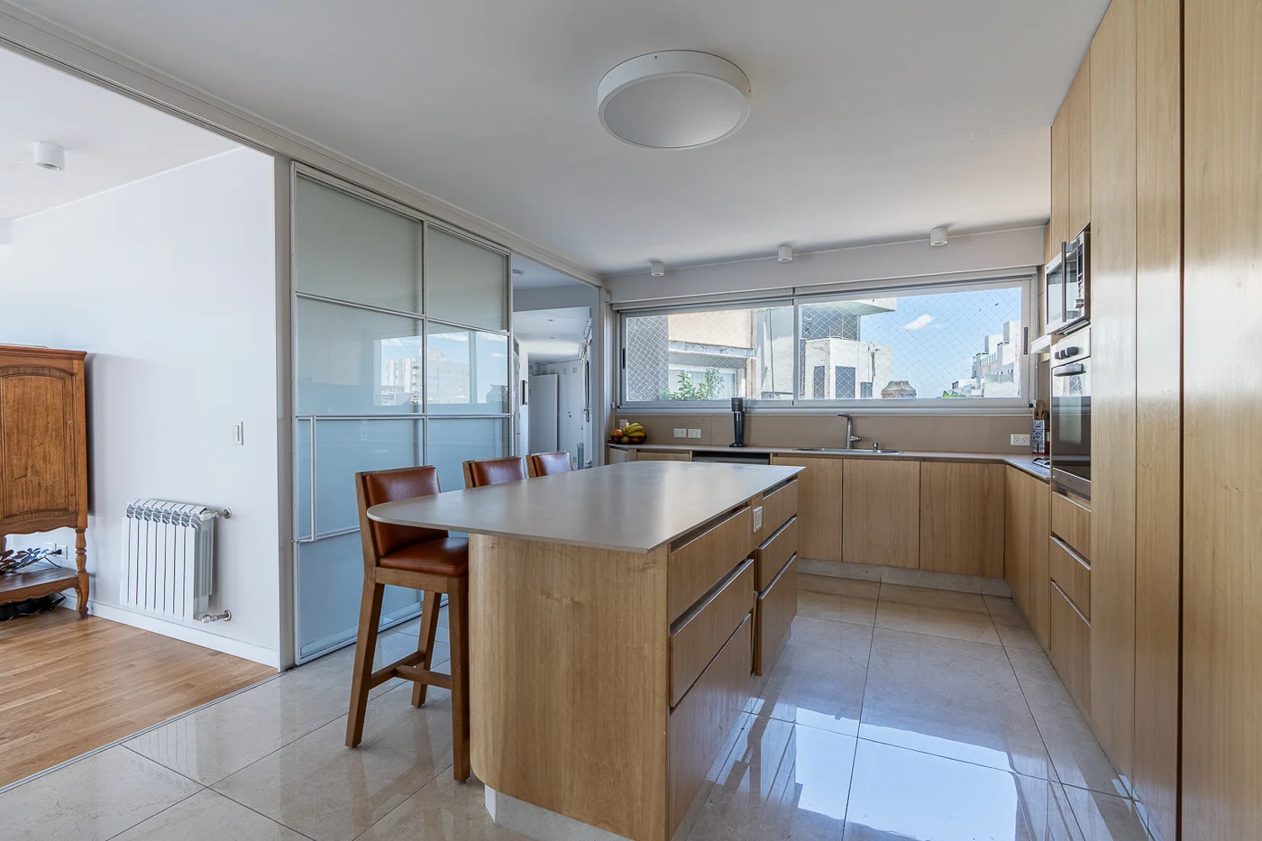 Cocina moderna con isla de madera clara y grandes ventanales.