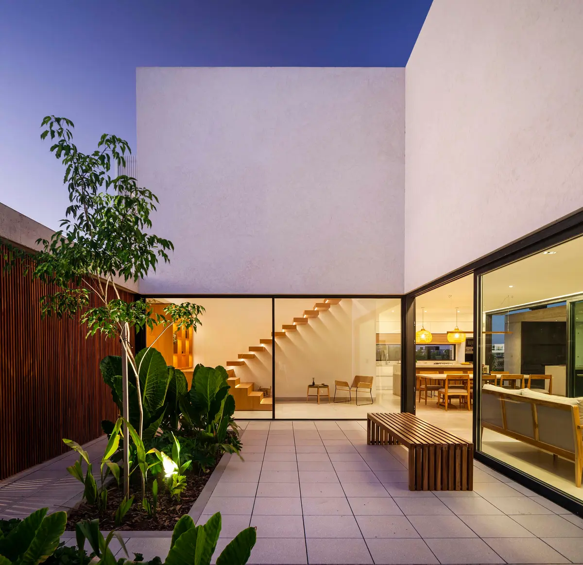 Patio moderno con vegetación exuberante y banco de madera — proyecto CASA J2M, por GMARQ, en Belén de Escobar