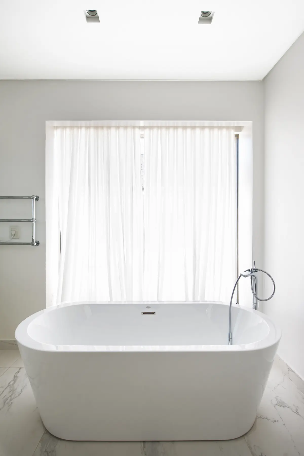 Banheiro moderno com banheira freestanding e cortinas brancas — projeto Casa DF, por Estudio Junor, em Tigre
