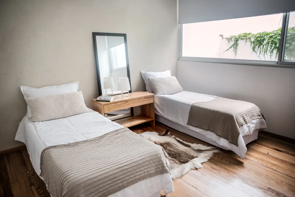 dormitorio moderno con dos camas, alfombra de piel y espejo — proyecto Ravignani, por Estudio Basa, en Palermo