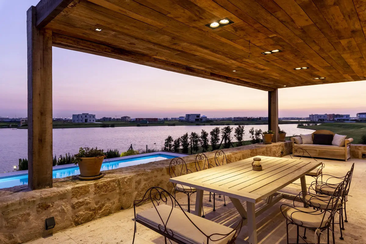 Varanda moderna com pérgola de madeira e vista para o lago — projeto Casa MF, por Estudio Junor, em Belén de Escobar
