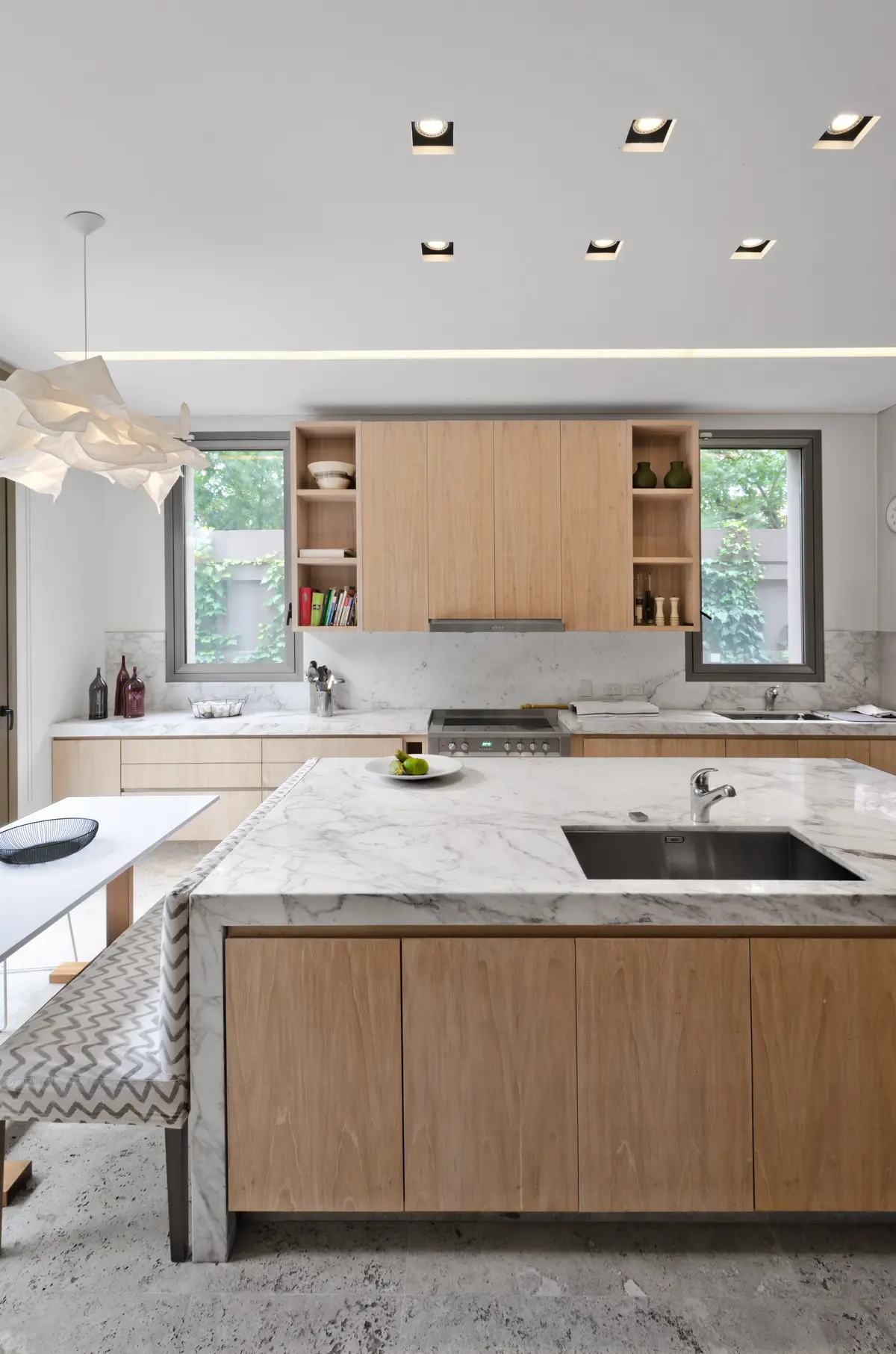 Cocina moderna con isla de mármol, muebles de madera clara y luz indirecta — proyecto Casa H, por Estudio Dado, en Belgrano