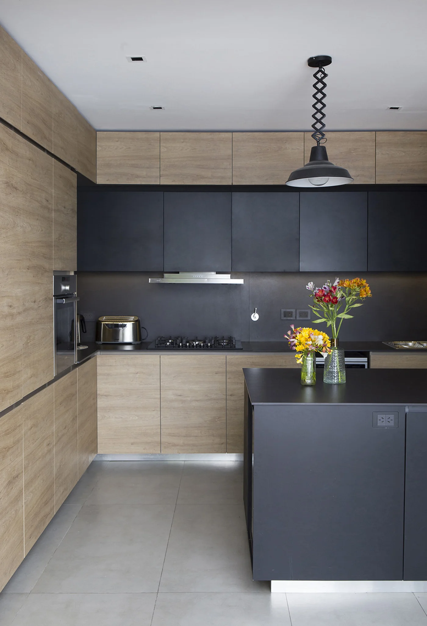 Cocina moderna con isla oscura, madera natural y luz colgante articulada.