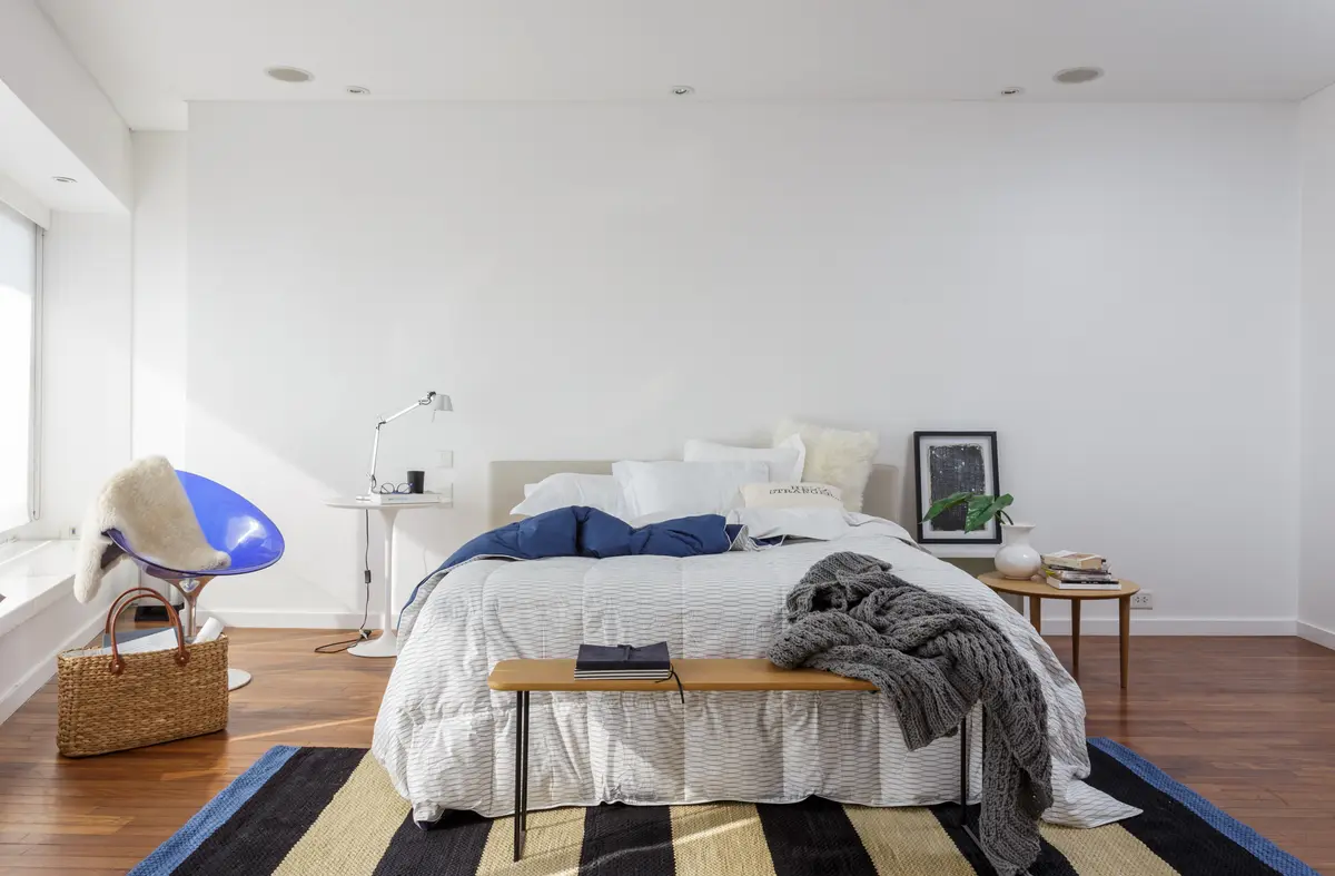 Dormitorio moderno con ventana de piso a techo y silla azul — proyecto Piso en Libertador III, por Gutman+Lehrer Arquitectas, en CABA