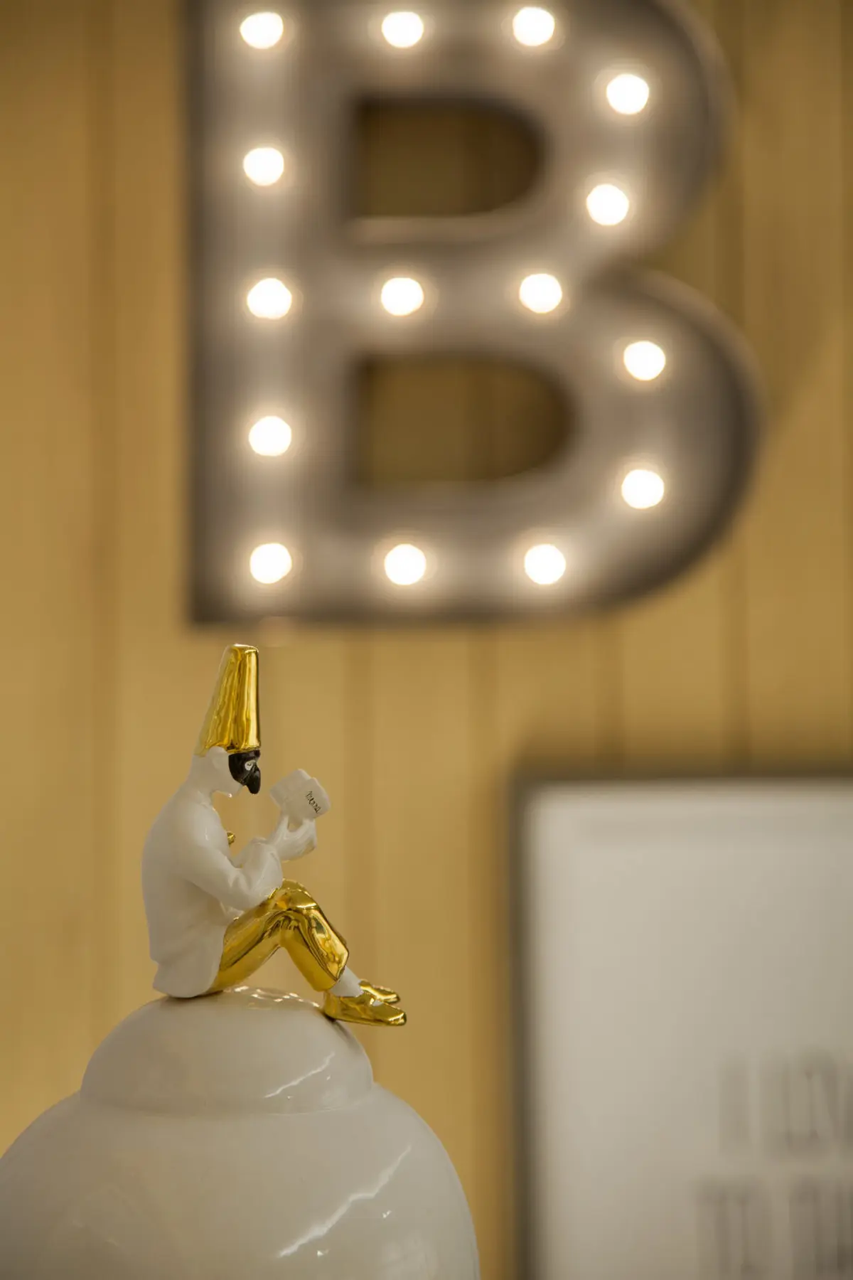 Escultura blanca con detalles dorados sobre fondo decorativo con letras luminosas — proyecto Quarto Bernardo, por Studio Ro-ca