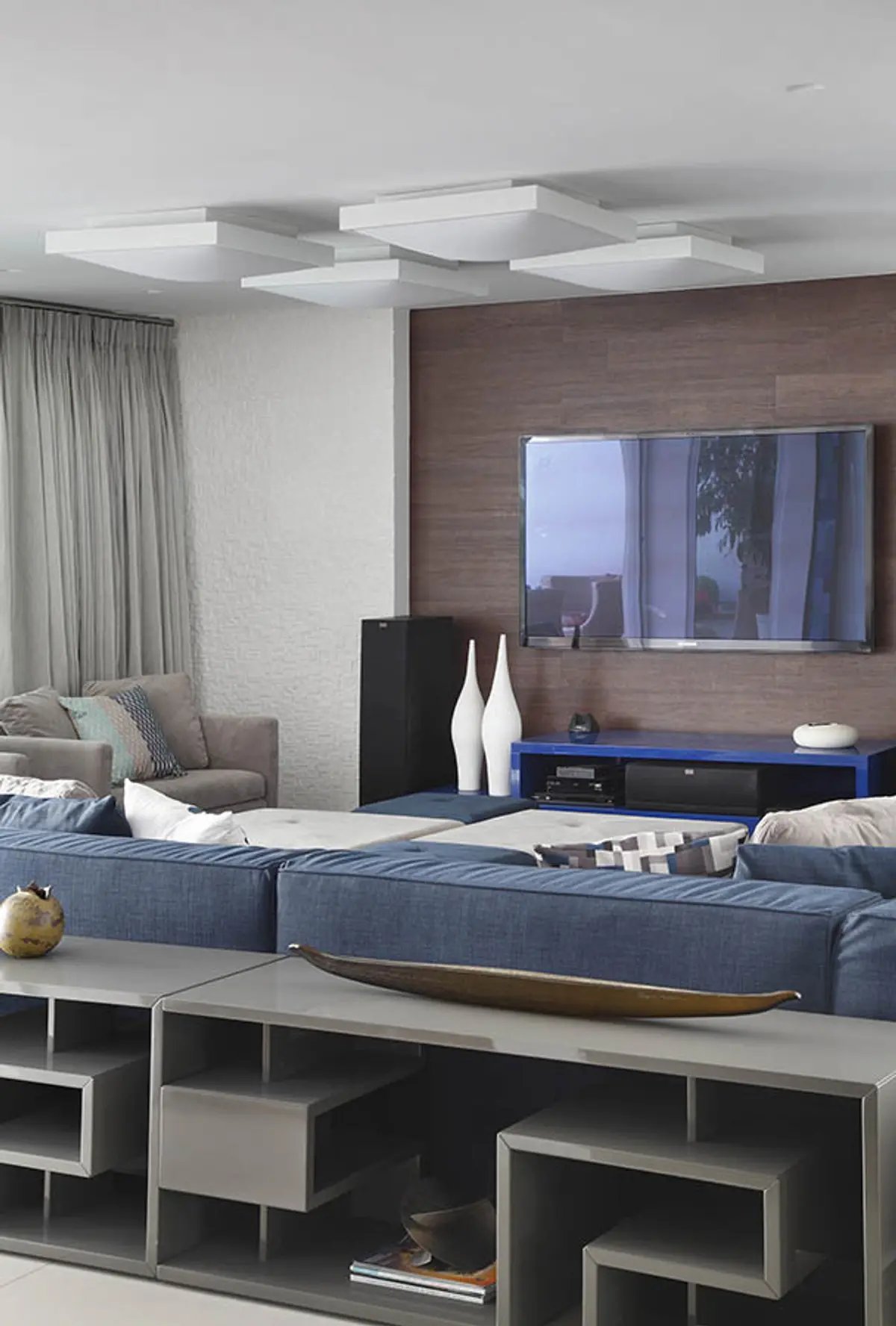 Living moderno con sofá azul, pared madera, TV empotrada y luces LED — proyecto Casa Barra ED, por Amanda Miranda