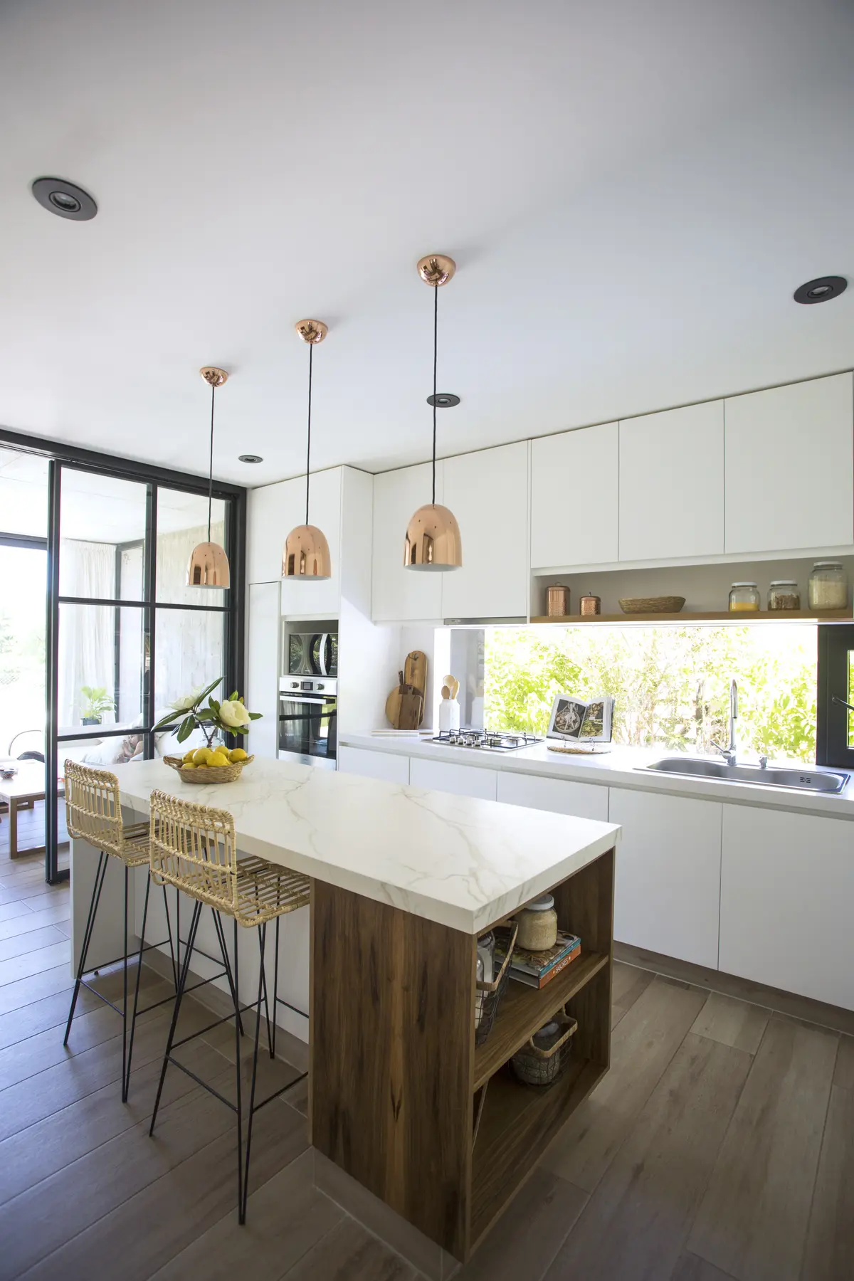 Cozinha moderna com ilha, bancos de vime e luminárias pendentes de cobre — projeto Casa Lion, por Estudio Lak