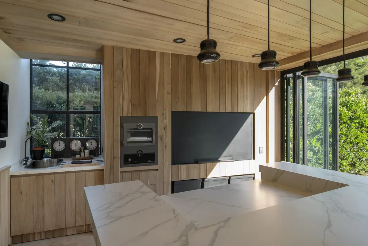 Cozinha moderna de madeira com ilha de mármore e janelas para a floresta — projeto Quincho PG, por Estudio Lak