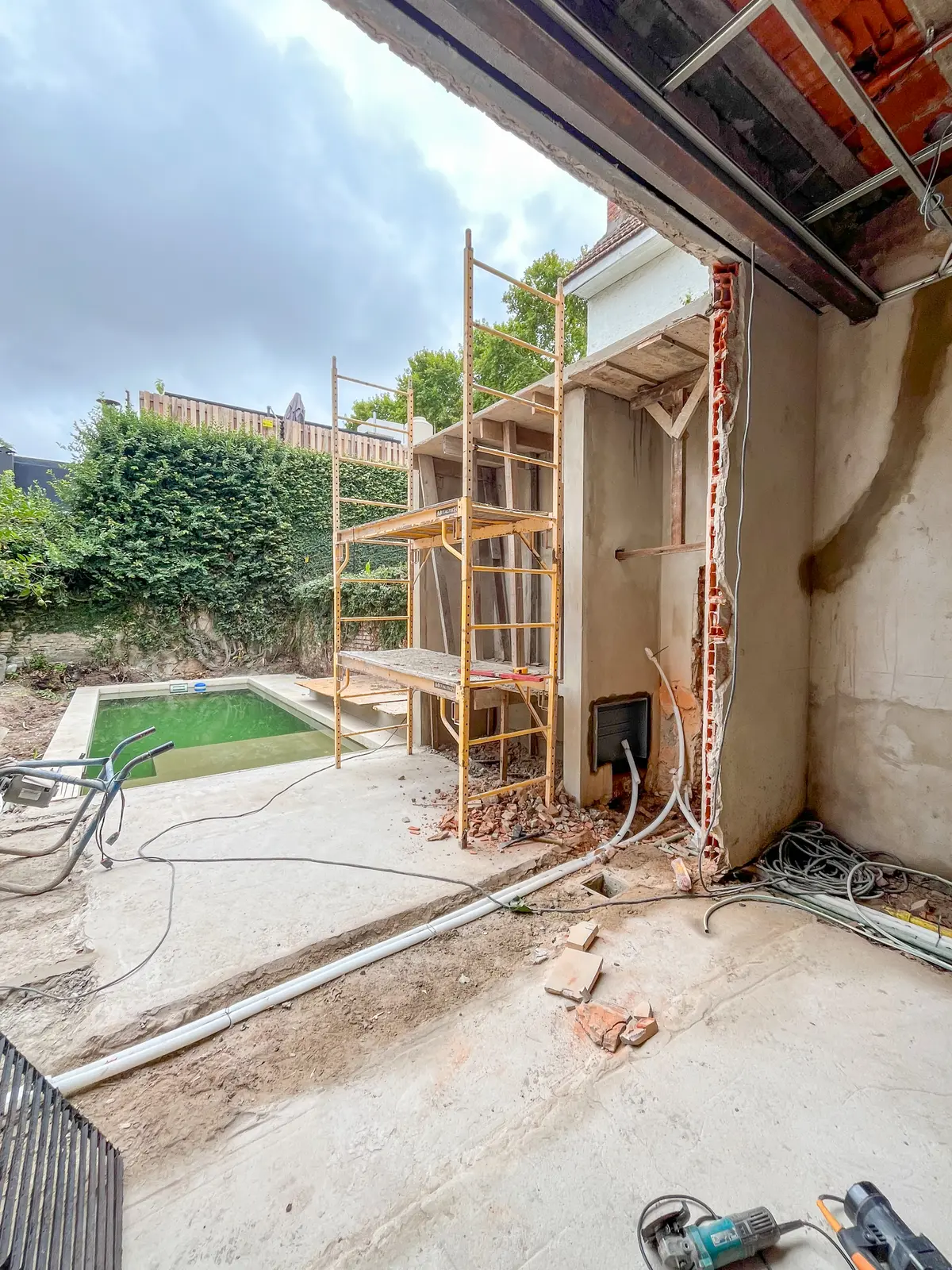 Zona de piscina en construcción con andamios y vegetación — proyecto Instalación de Sistema Multisplit y Radiadores Acassuso, por Climatizacion HD, en B1641 Acassuso