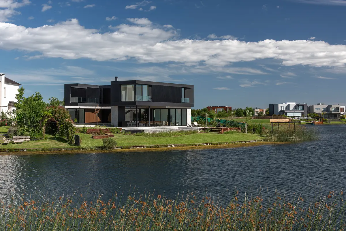 casa moderna preta em frente ao lago com janelas amplas — projeto CASA MUELLES, por GMARQ, em Escobar