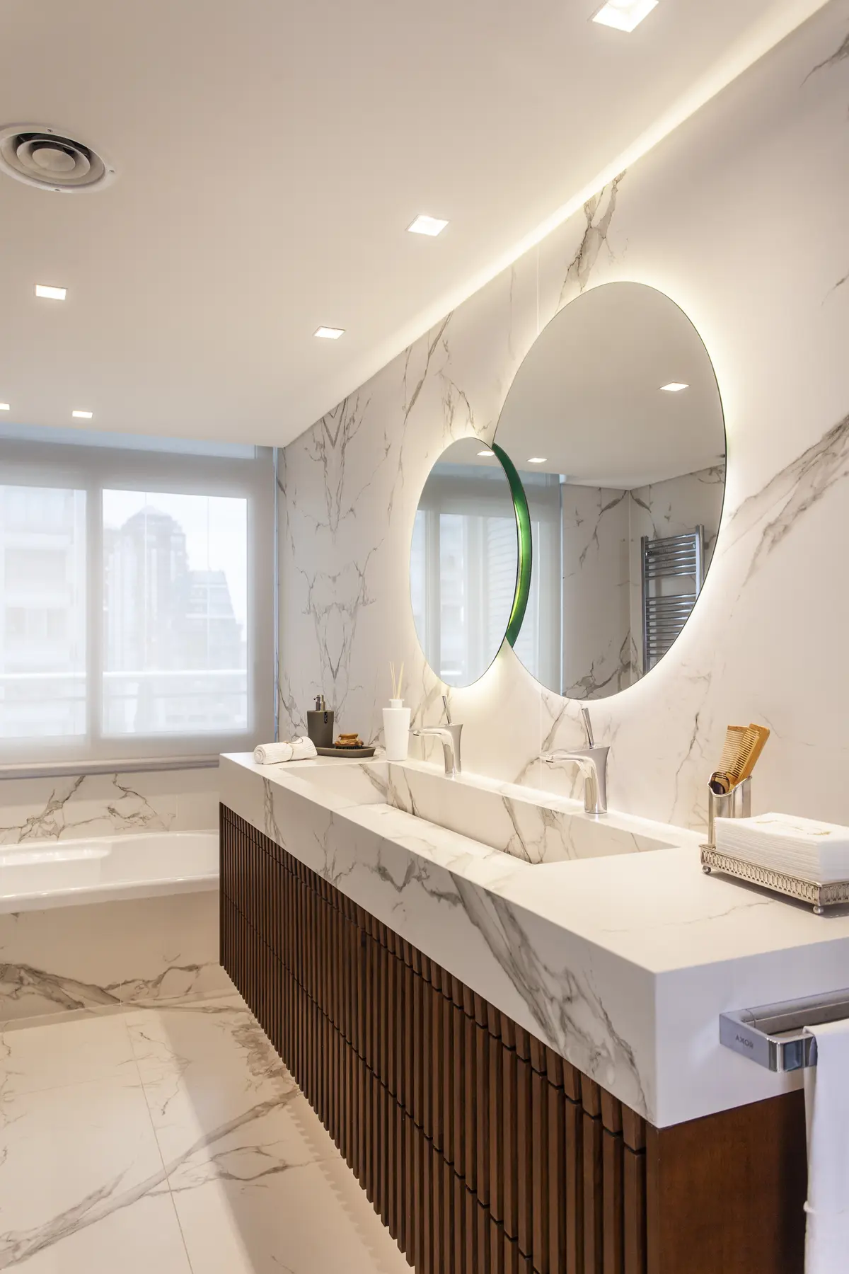 Baño moderno con mesada integrada de mármol, espejo ovalado retroiluminado y revestimiento de madera — proyecto Pacífico BRT, por Vanguarda Arquitectos, en CABA