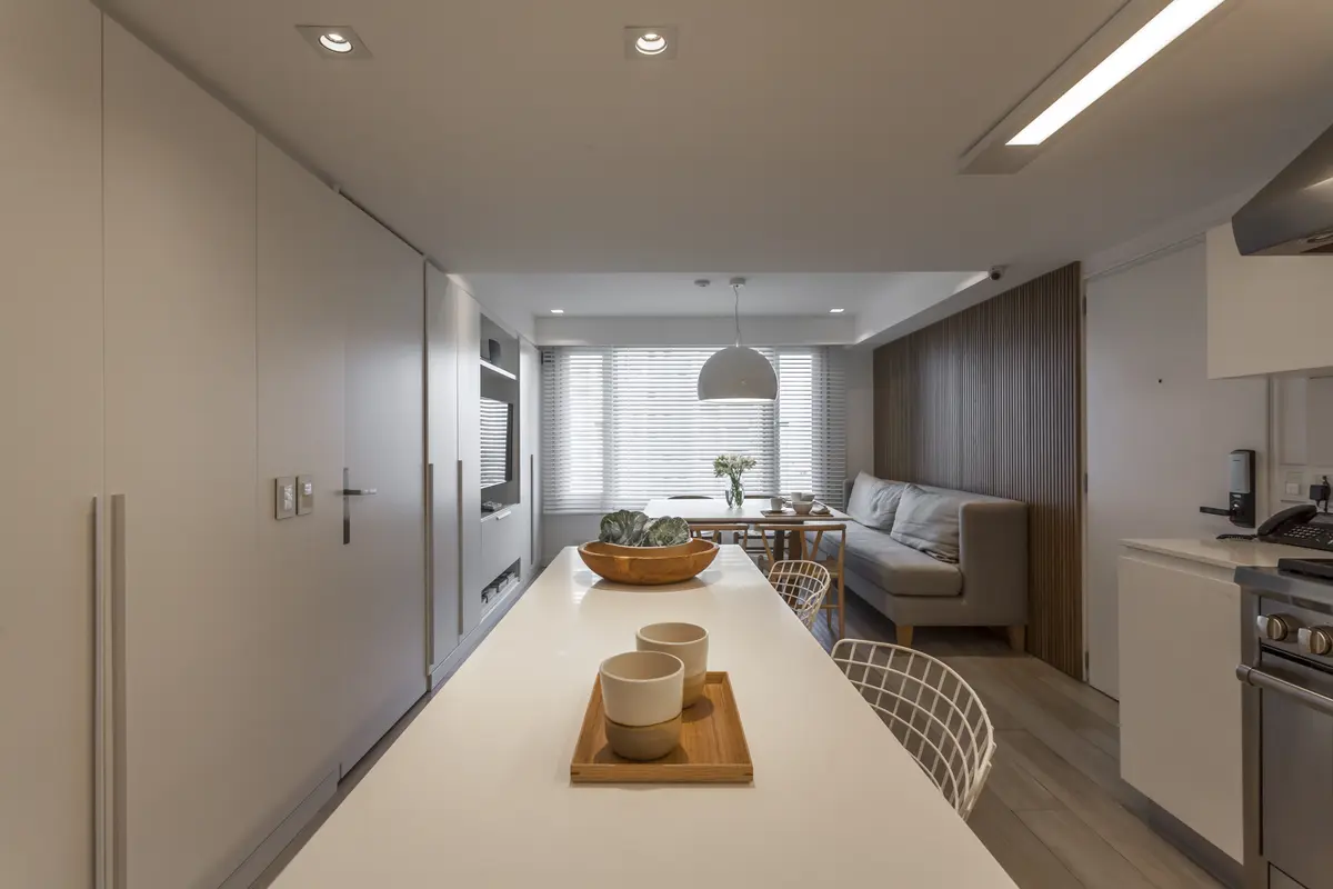Cocina moderna integrada con isla, isla blanca y pared de listones de madera — proyecto Le Parc, por Judith Babour, en CABA