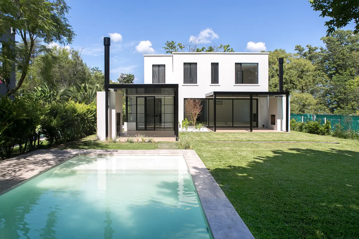 Casa moderna branca com piscina e amplas janelas em um ambiente verde — projeto Bosque Chico, por Estudio Arq. María Sioli, em Garin