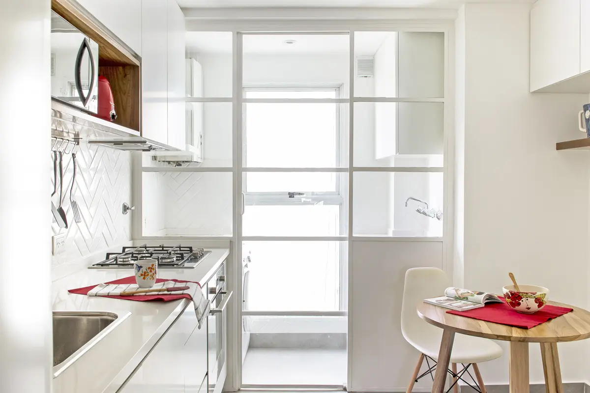 Cocina moderna con gabinetes blancos, piso de madera clara y puertas corredizas de vidrio — proyecto Oro, por Estudio Arq. María Sioli, en CABA