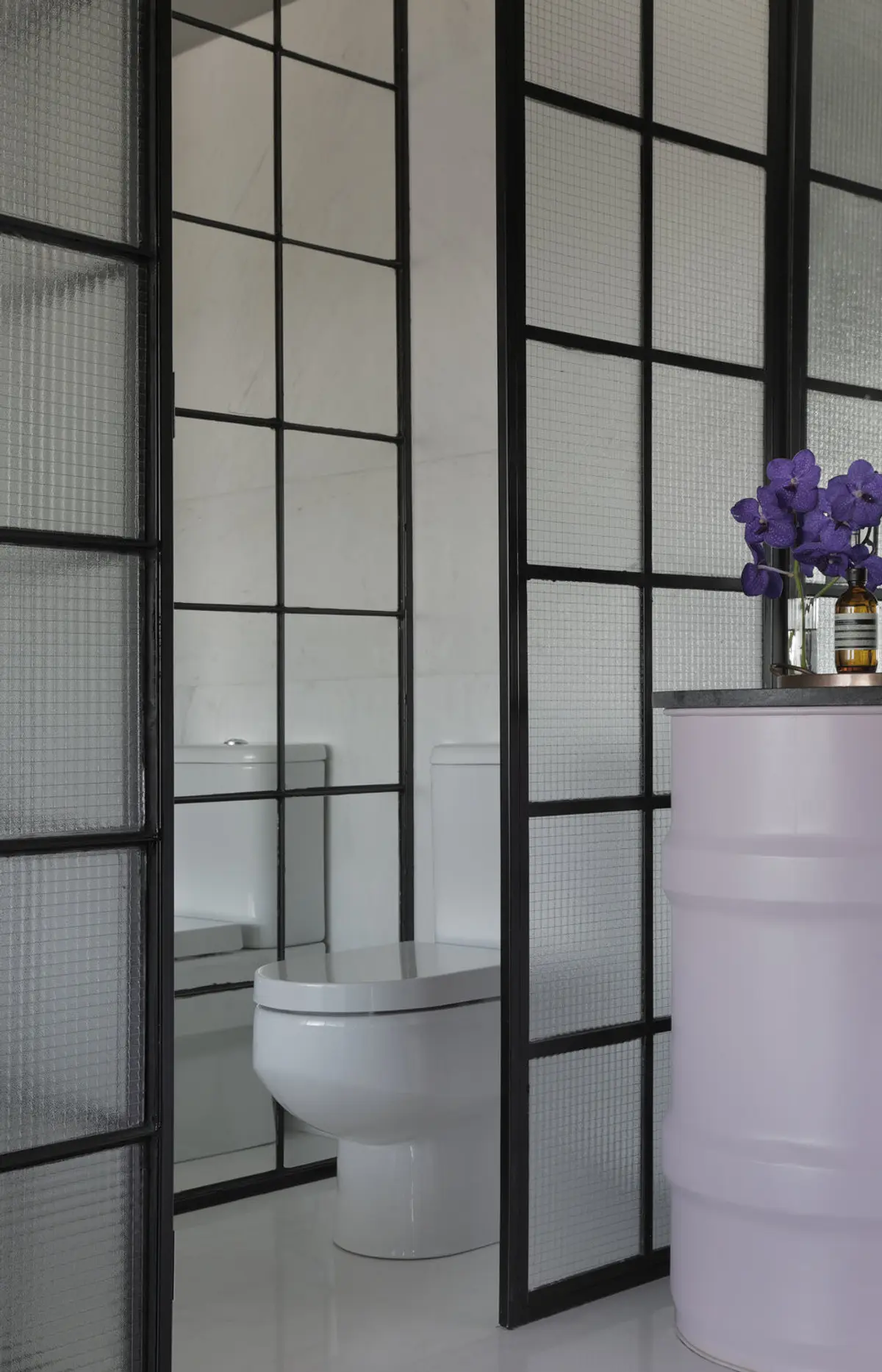 Toilette minimalista con puerta vidrio y marco negro, flores violetas — proyecto RA Loft, por Studio Ro-ca